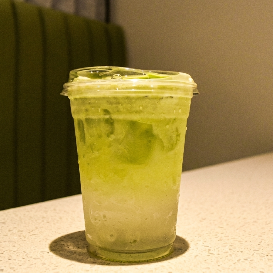 Clear plastic cup of iced green matcha drink on a speckled countertop in a warmly lit restaurant interior.