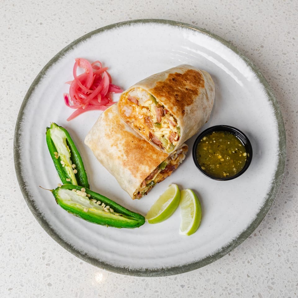 Grilled burrito stuffed with eggs, cheese, vegetables, and bacon, served with pickled onions, jalapeños, lime wedges, and green salsa.